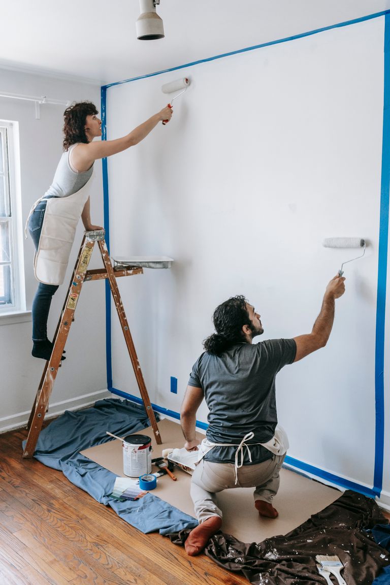 A couple collaborates on painting a white wall in their new home, demonstrating teamwork and renovation.