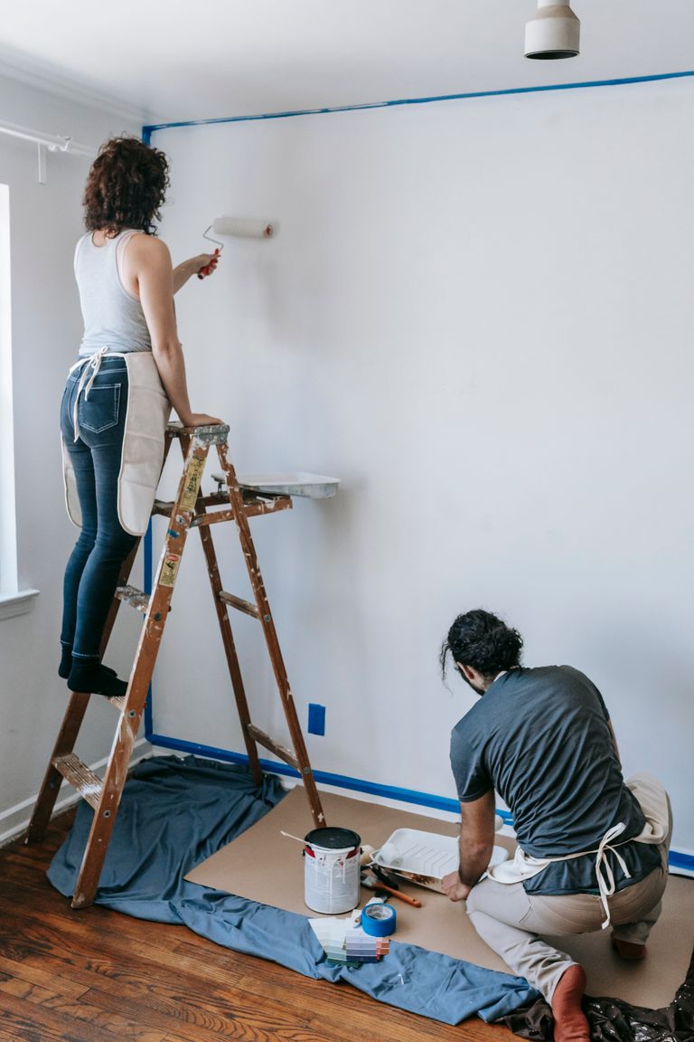 A couple working on a home renovation project, painting a room with rollers.